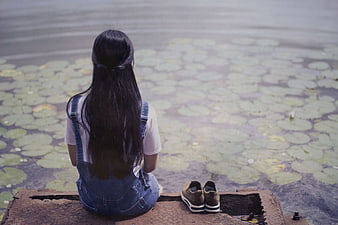Girl sitting by pond with lily pads looking away