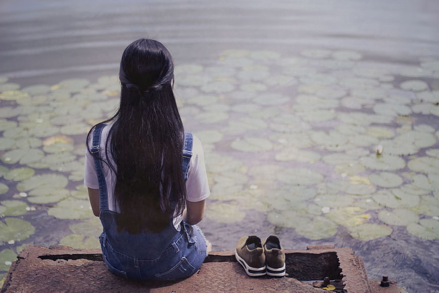 Girl sitting by pond with lily pads looking away