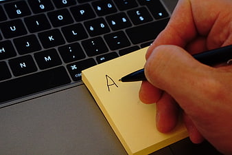 Hand writing letter A on yellow sticky note next to laptop keyboard