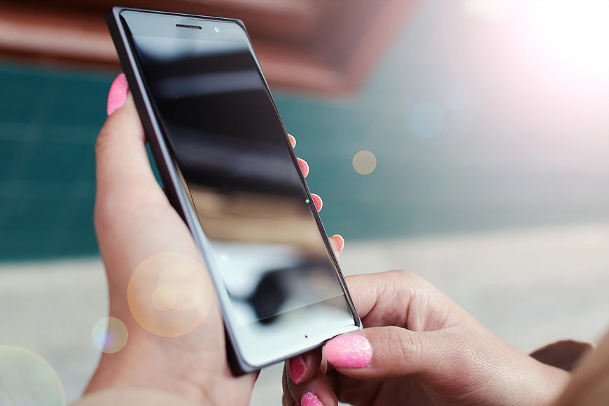 Woman holding black smartphone with pink nails by pool