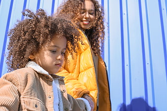 Mother and daughter with curly hair against blue wall