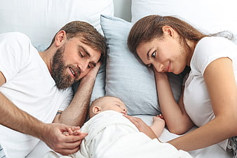 Happy Parents Watching Sleeping Newborn Baby in Bed