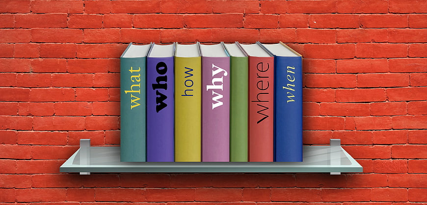 Colorful Books with Question Words on Shelf Against Red Brick Wall
