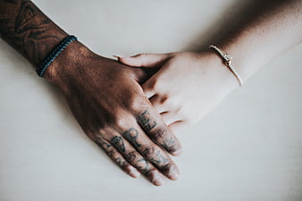 Interracial couple holding hands with tattoos and bracelets