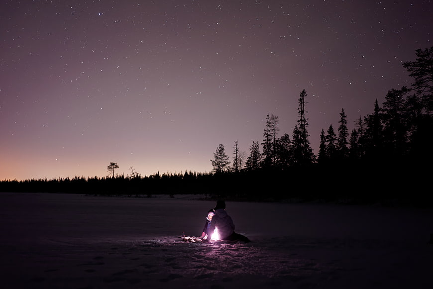 Couple sitting in snow under starry night sky