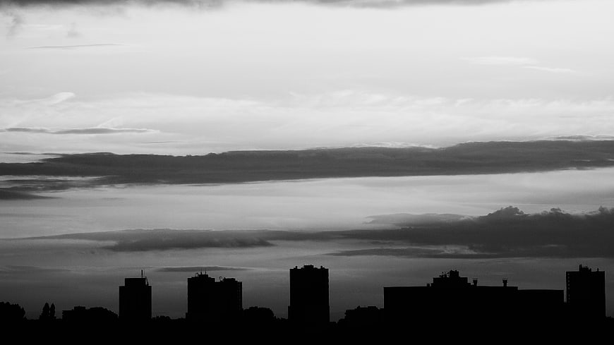 Black and white silhouette of city skyline against dramatic cloudy sky