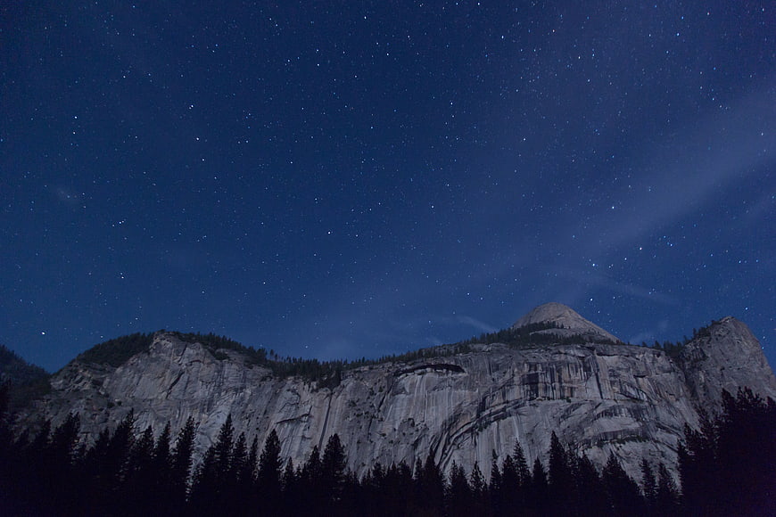 Starry Night Sky Over Granite Mountain Cliffs and Pine Forest
