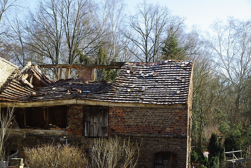 Abandoned brick house with damaged roof in winter woods