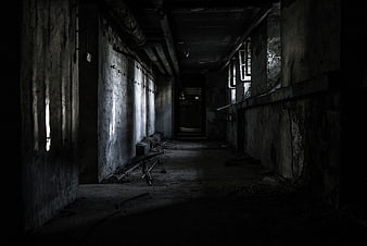 Dark abandoned concrete hallway with peeling walls and debris