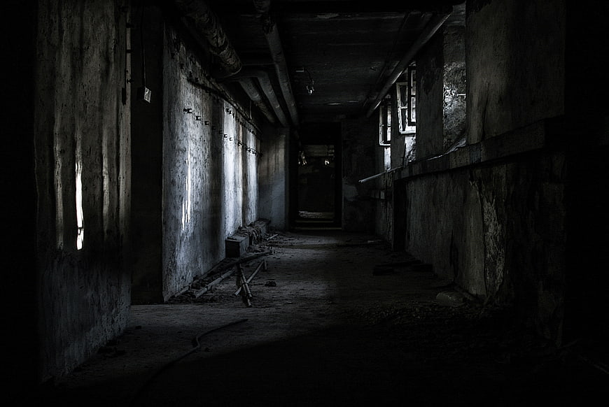 Dark abandoned concrete hallway with peeling walls and debris