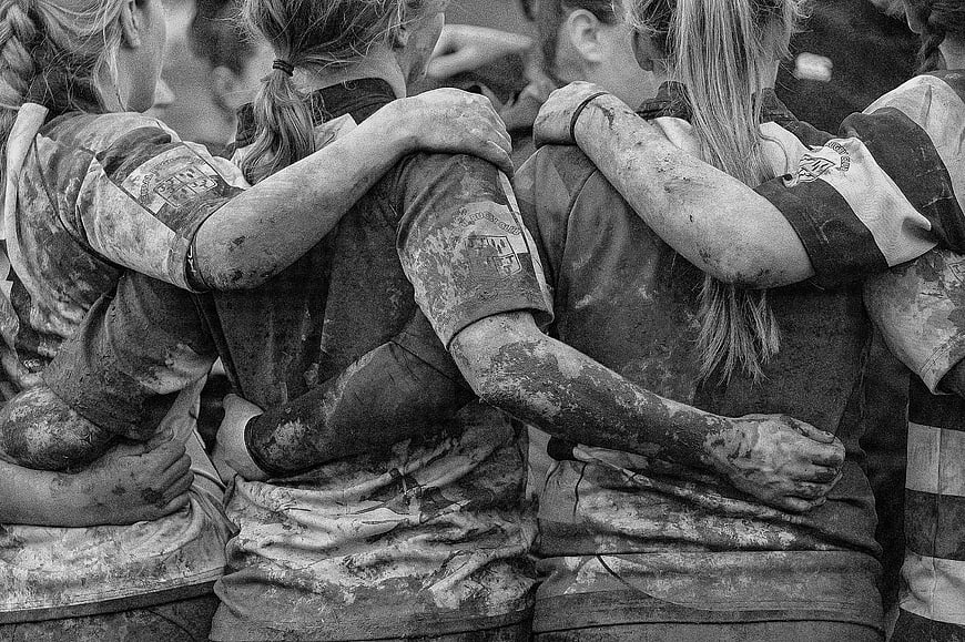 Muddy female athletes hugging in a tight team huddle