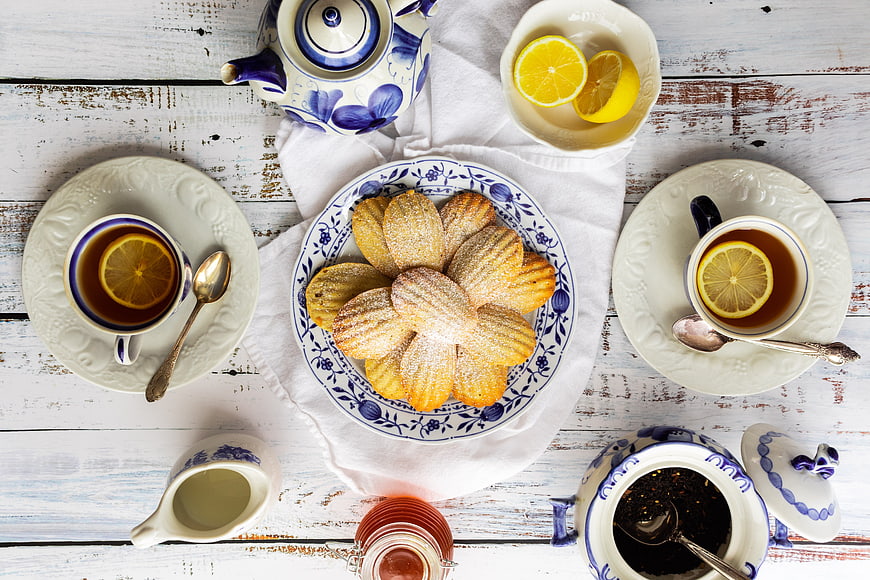 Top view of madeleine cookies with tea and lemon on rustic table