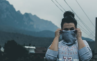 Woman Pulling Hoodie Over Face Against Mountain Background