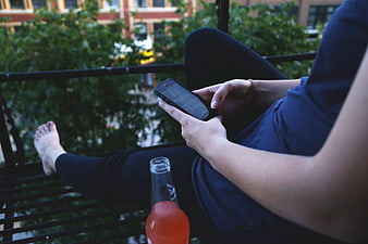 Woman relaxing on balcony with smartphone and drink