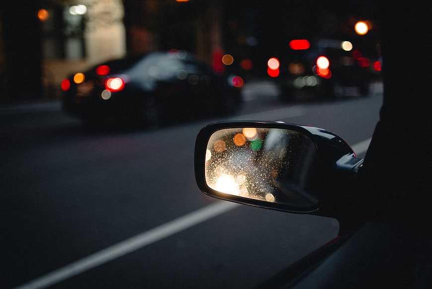 Car side mirror with raindrops reflecting city lights at night