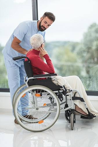 Male nurse comforting elderly woman in wheelchair by window