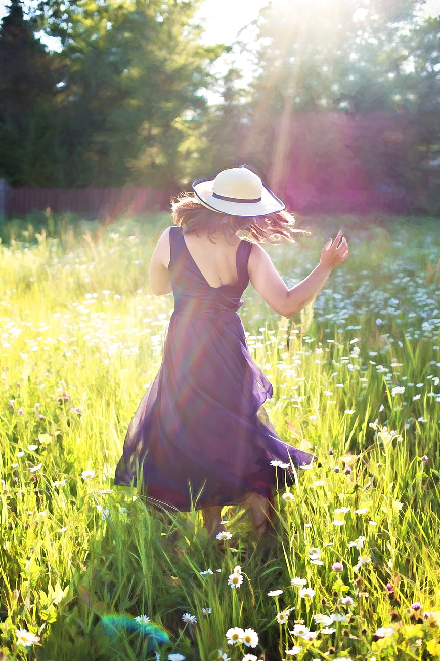 Woman in purple dress and hat dancing in a sunny meadow