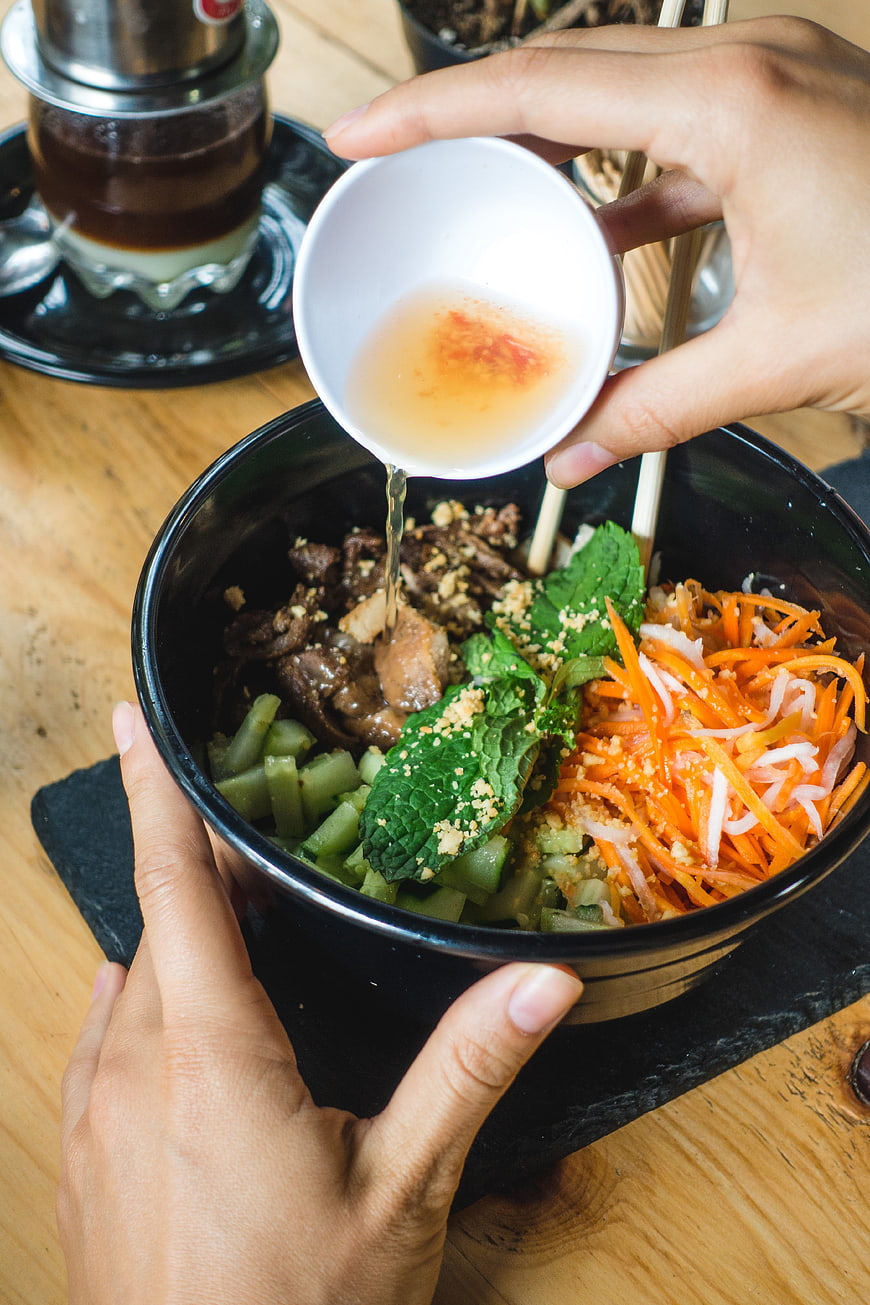 Hands pouring sauce on Vietnamese beef noodle bowl
