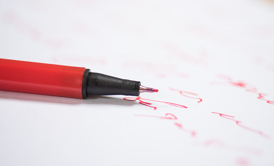 Red pen writing on white paper with shallow depth of field