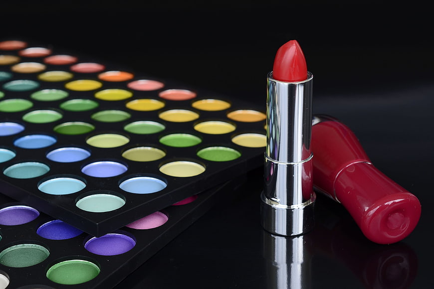 Red lipstick and colorful eyeshadow palette on black background