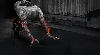 Athlete with fiery arms pushing heavy tire in dark gym