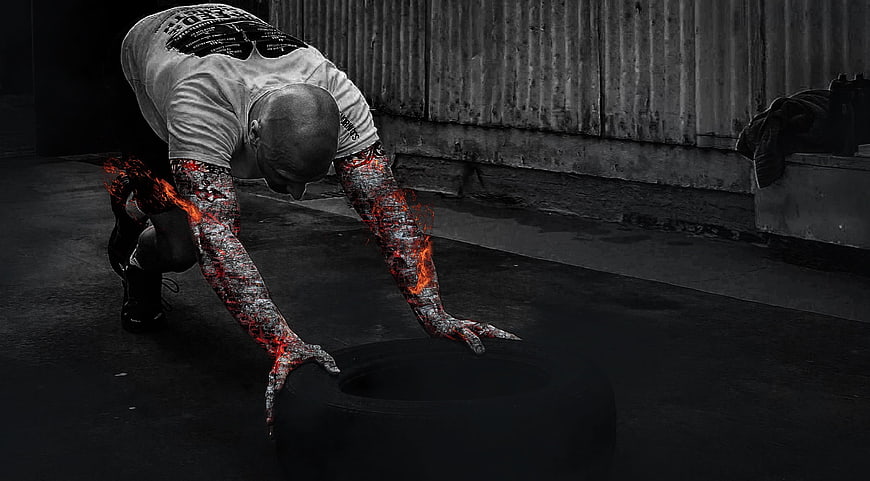 Athlete with fiery arms pushing heavy tire in dark gym