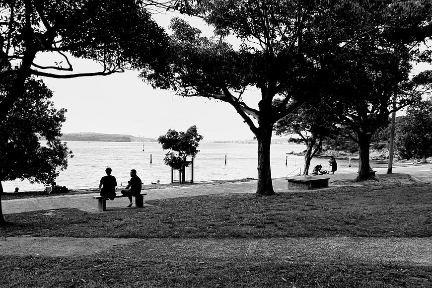 Black and white photo of couple sitting on park bench by water