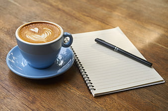 Blue Coffee Cup with Latte Art Beside Notebook and Pen