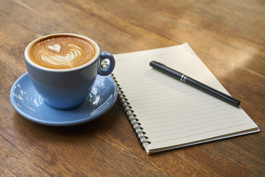Blue Coffee Cup with Latte Art Beside Notebook and Pen