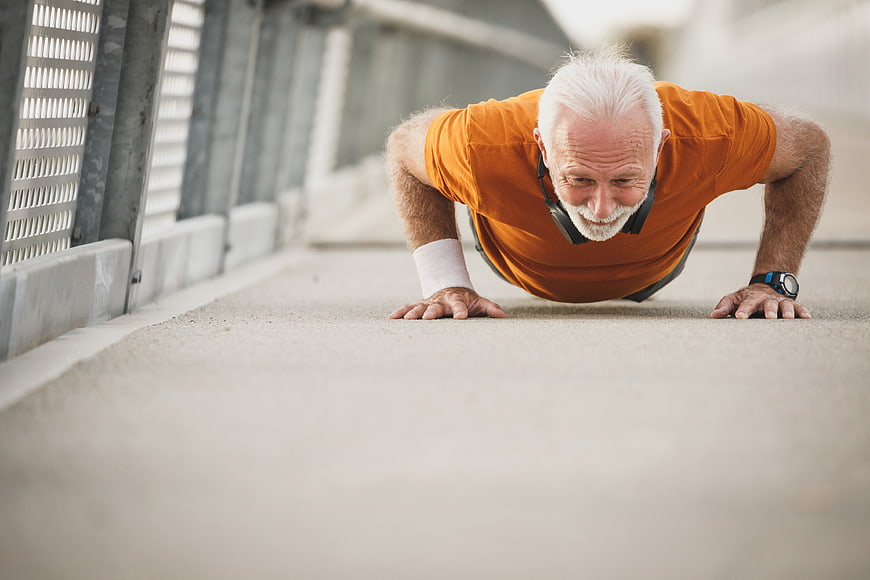 Senior man doing push-ups outdoors in orange shirt