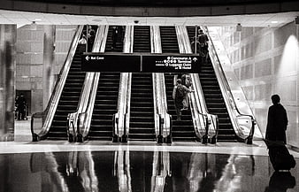 Black and white airport escalators with travelers and luggage