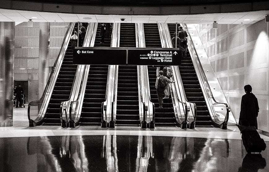 Black and white airport escalators with travelers and luggage