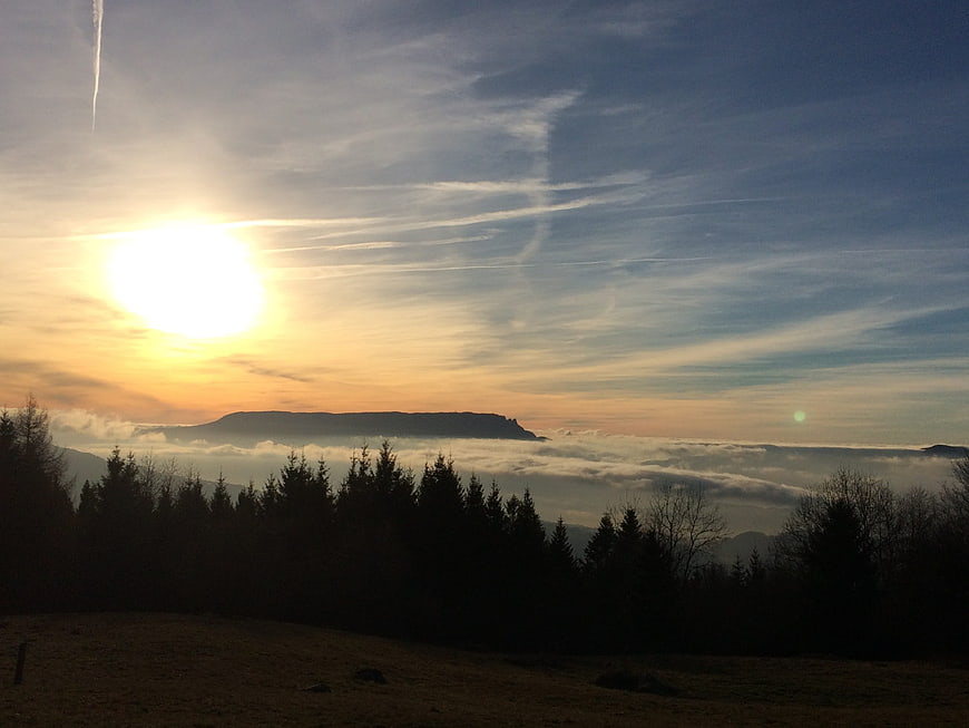 Sunset over mountain ridge with sea of clouds and forest silhouette