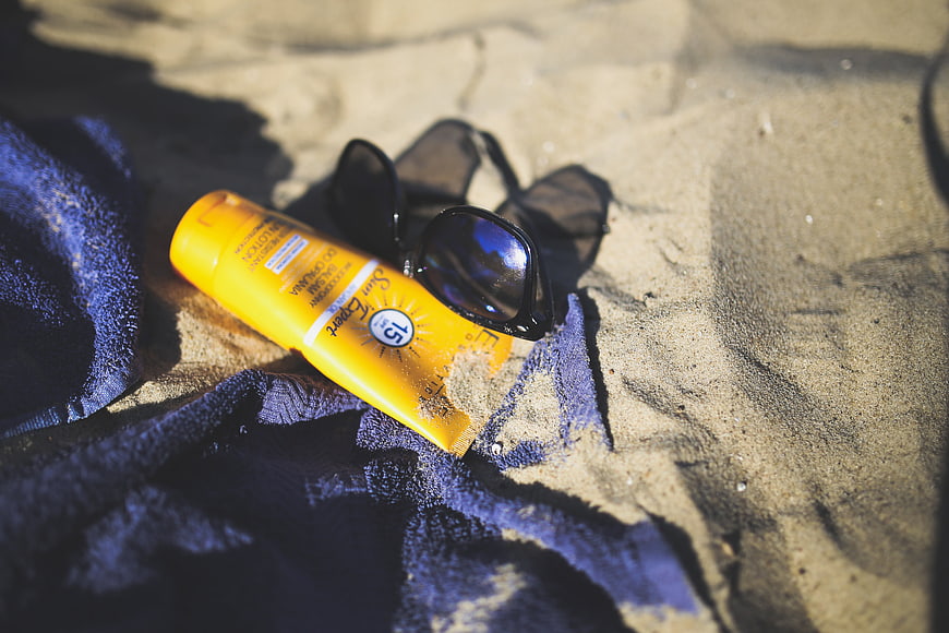 Sunscreen Bottle And Sunglasses On Beach Towel