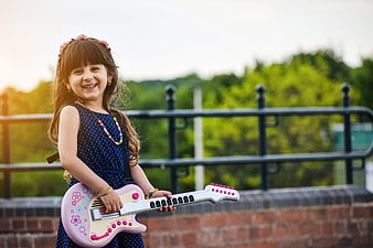Happy little girl playing pink toy guitar outdoors