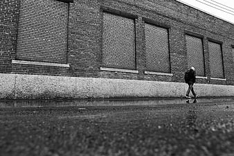 Man Walking Past Brick Wall in Black and White
