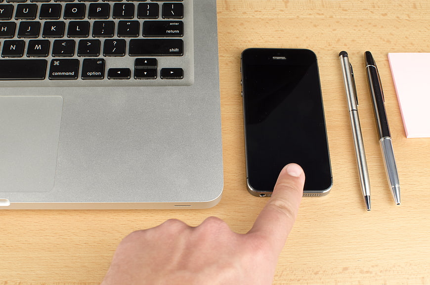 Hand pointing at smartphone screen on wooden desk with laptop