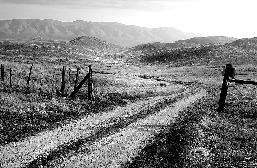 Black and White Dirt Road Winding Through Rolling Hills