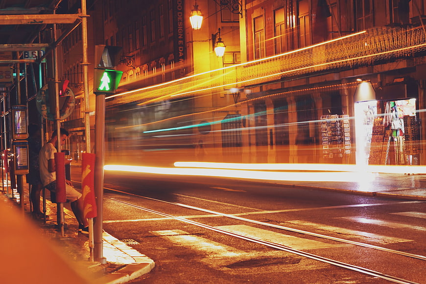 Night street scene with tram light trails and waiting passengers
