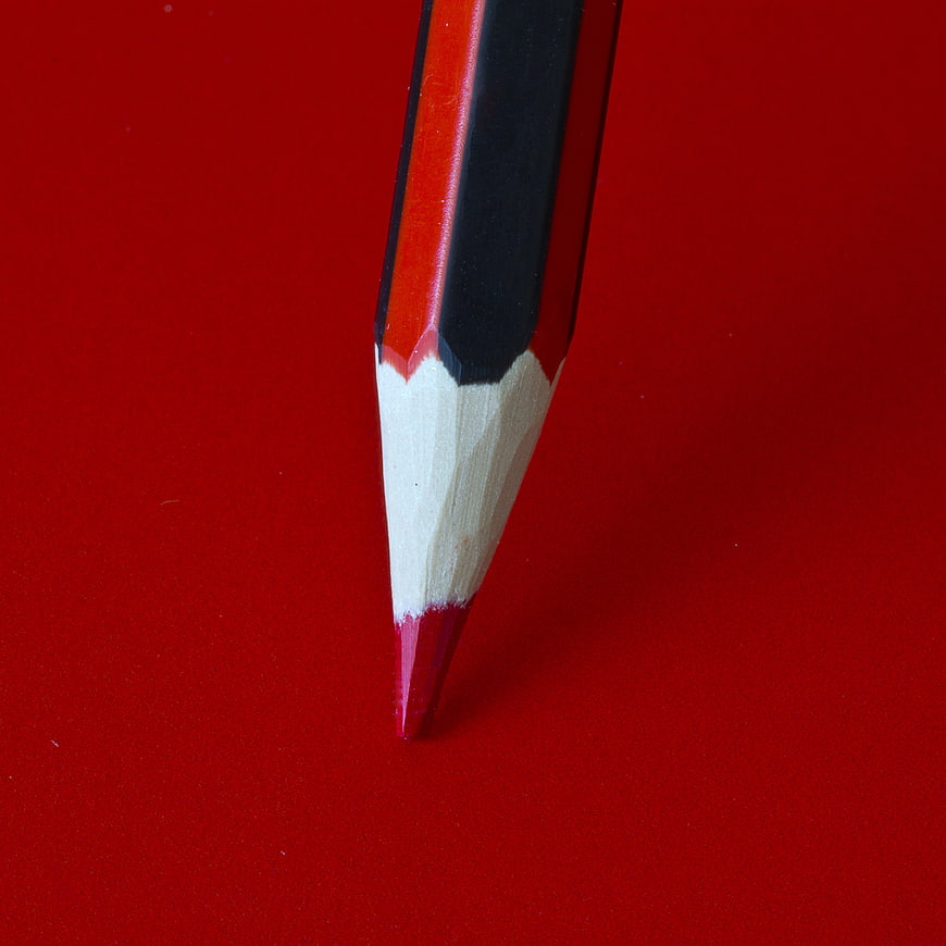 Close-up of a sharp red and black pencil on a red background