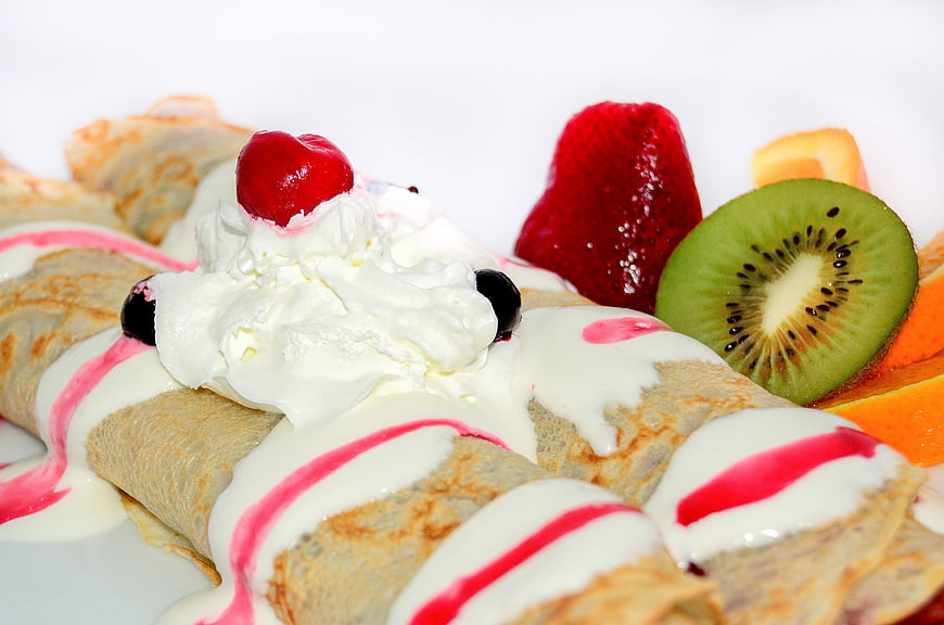 Rolled crepes with whipped cream, fresh fruit, and berry sauce