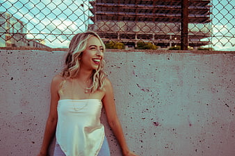 Happy blonde woman laughing against urban concrete wall