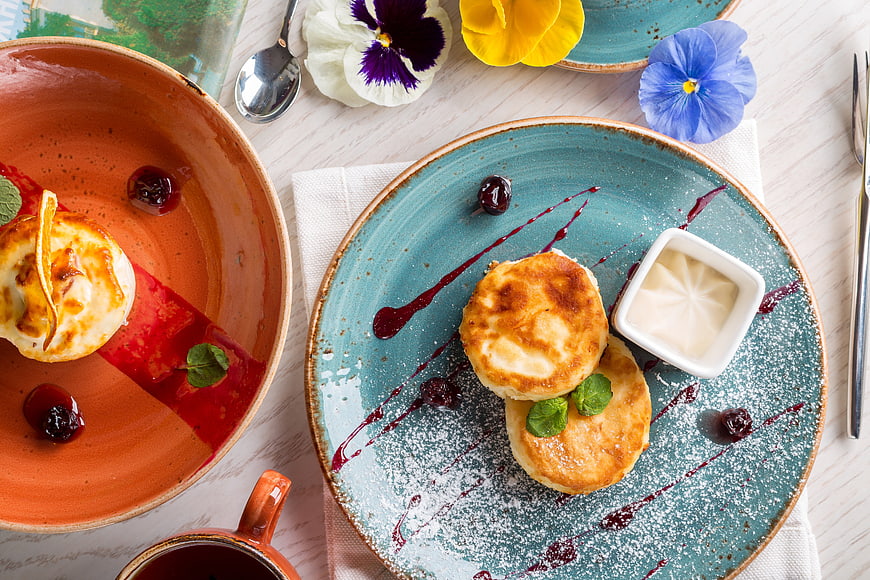 Overhead view of syrniki pancakes with berry sauce and flowers