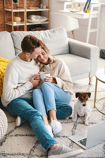 Young couple cuddling on living room floor with dog and coffee