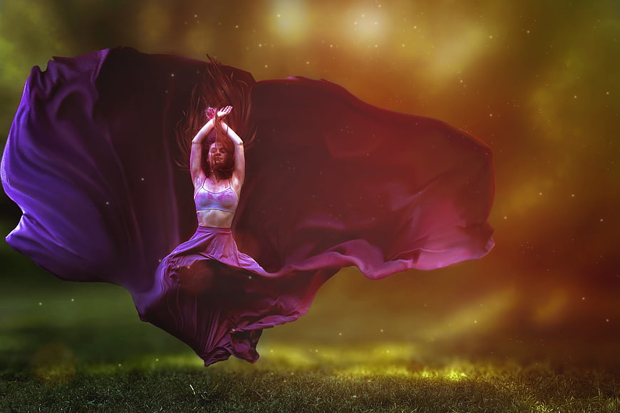 Woman dancing with flowing purple fabric in golden light