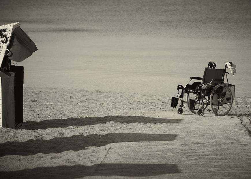 Empty Wheelchair on Beach Path with Long Shadows