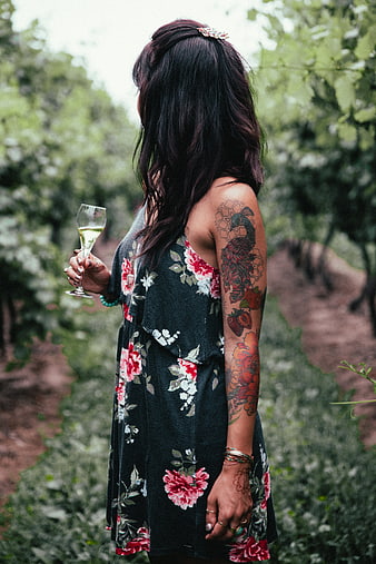 Woman with tattoos holding wine glass in vineyard