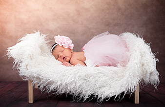 Sleeping newborn baby girl in pink tutu on white fur