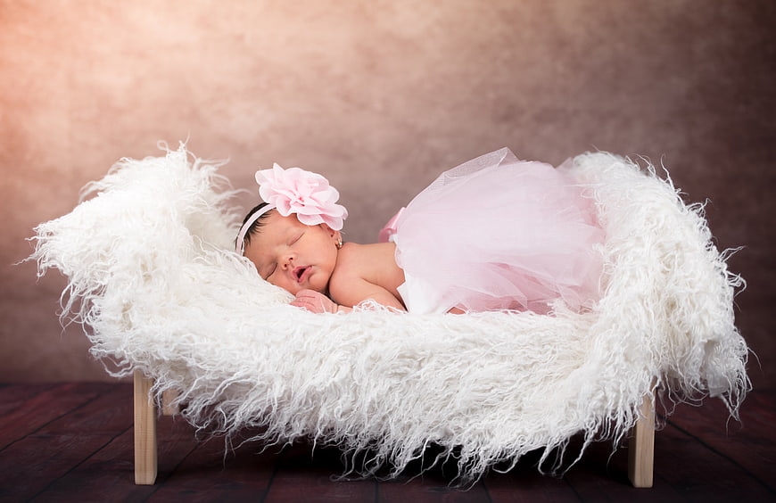Sleeping newborn baby girl in pink tutu on white fur