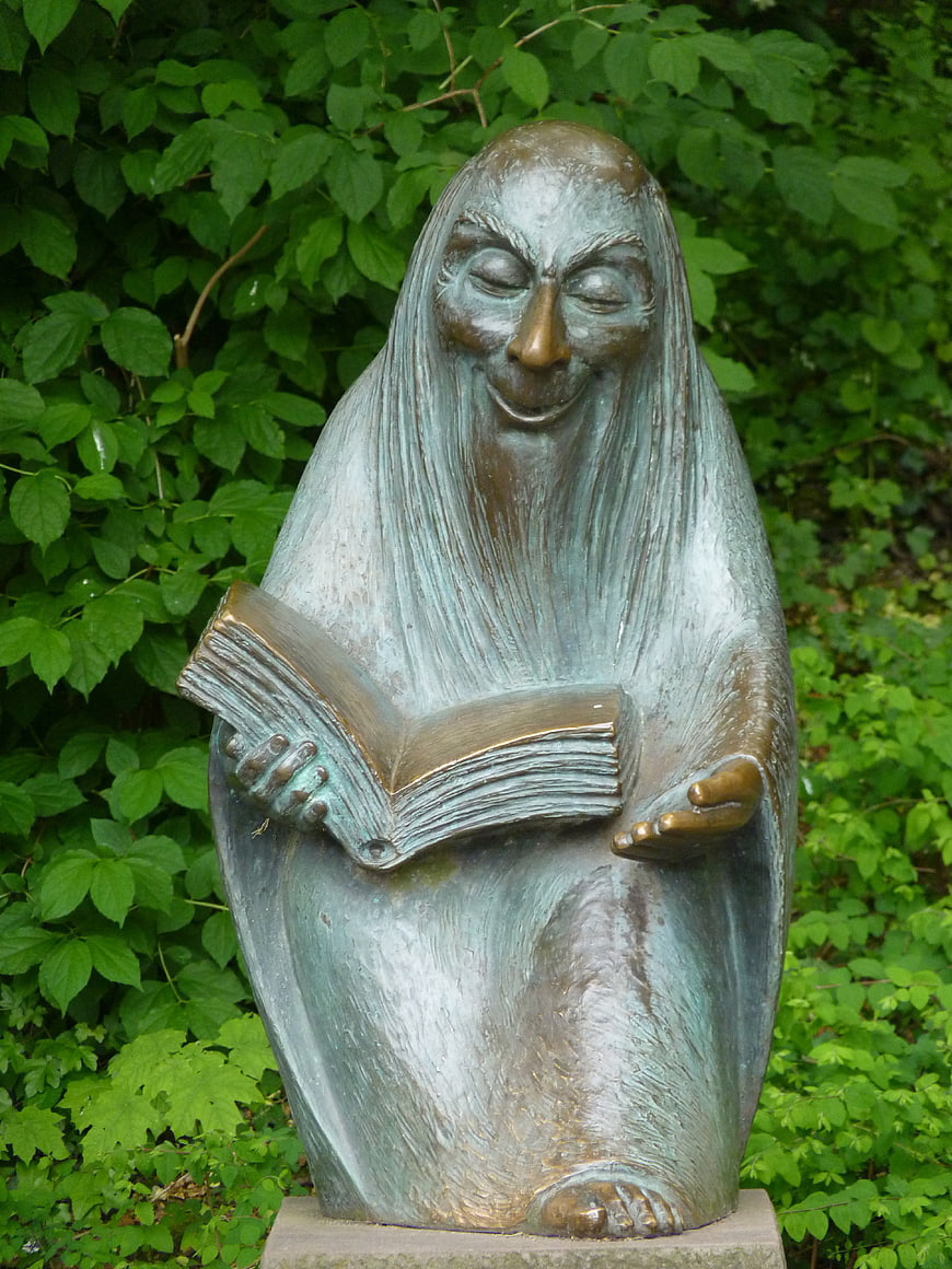 Bronze statue of a smiling figure reading a book in a garden